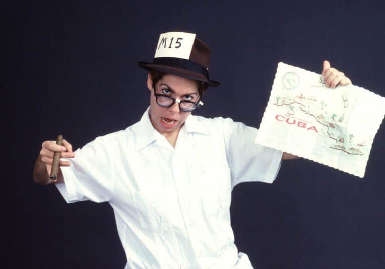 Photo shows Carmelita in drag as Pingalito character holding placemat with Map of Cuba.