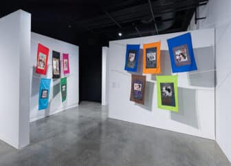 Ten brightly colored textile works hung with clothespins on stacked clotheslines that form four rows across two adjacent walls.